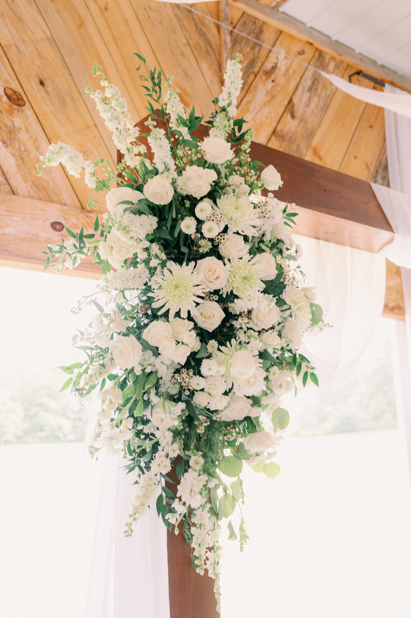 Elegant white floral arrangement with roses and greenery decorating a wooden arch at a Huntsville wedding ceremony venue.