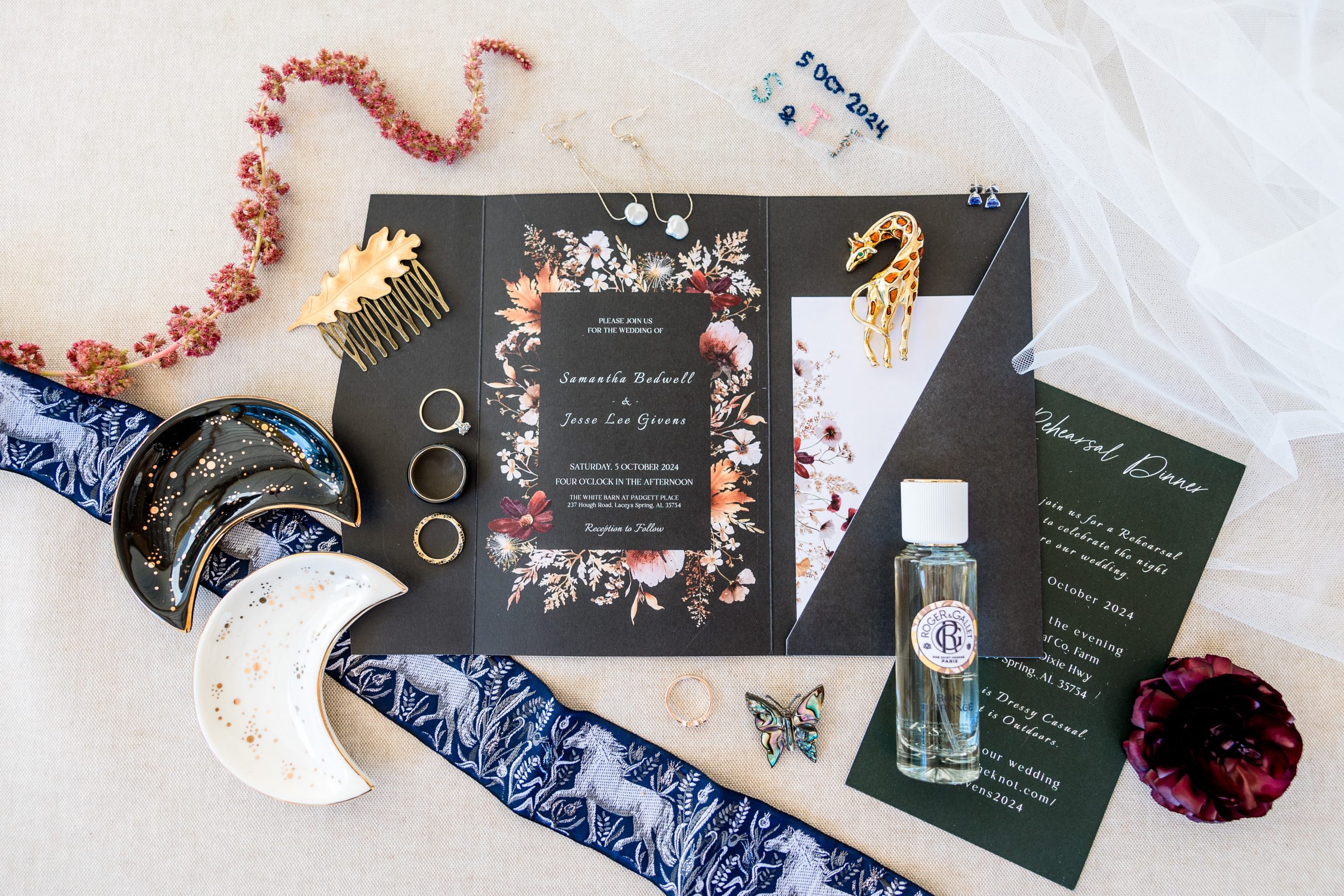 Flat lay of wedding invitation suite, rings, jewelry, and keepsakes styled with floral accents and personal details.