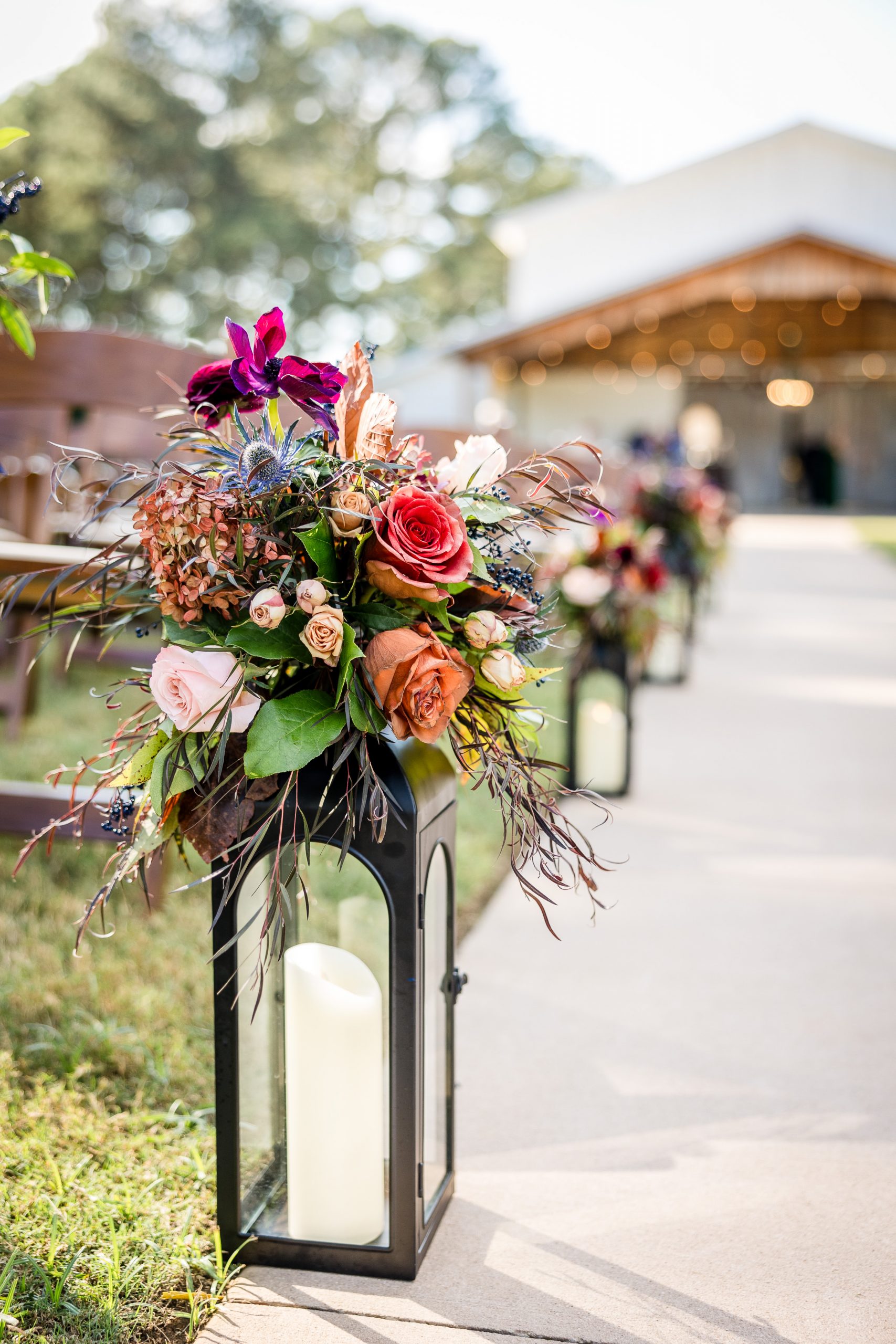 Lantern with lush floral arrangement featuring roses and hydrangeas lining the wedding ceremony aisle at a Huntsville venue.